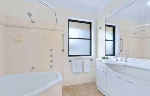 Baño blanco con bañera y lavamanos en Stay At Raffertys Resort, en Swansea
