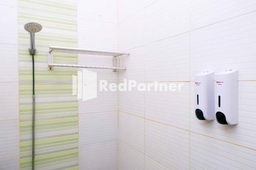 a white tiled bathroom with a shower with blackippers at Hotel Permata Makassar Mitra RedDoorz in Balangberu