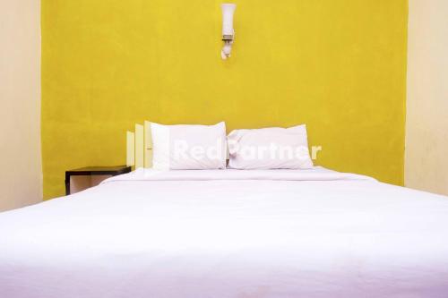 Hotel Permata Makassar Mitra RedDoorz في Balangberu: غرفة نوم بسرير ابيض بجدار اصفر