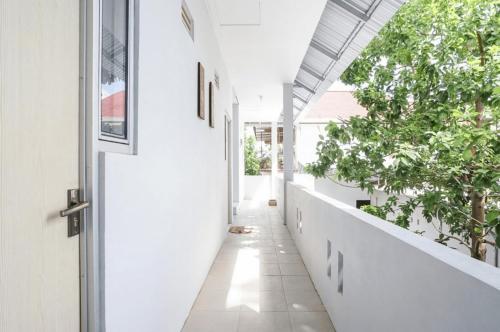 a hallway with white walls and a door and trees at PAS Residence Sam Ratulangi Airport Mitra RedDoorz in Mapanget