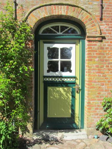 eine grüne Tür mit einem Fenster in einem Backsteingebäude in der Unterkunft Historischer Davidshof - Mit dem Rad die Nordseehalbinsel erkunden in Oldenswort