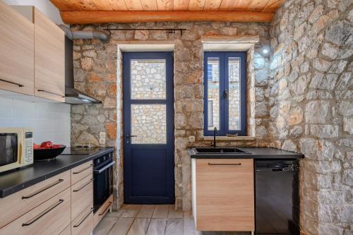 a kitchen with a blue door and a stone wall at Manousaki in Lambiní