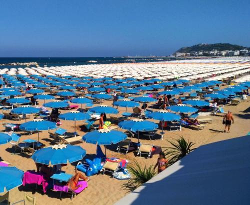 a beach with blue umbrellas and people on it at Hotel HamilTown in Cattolica