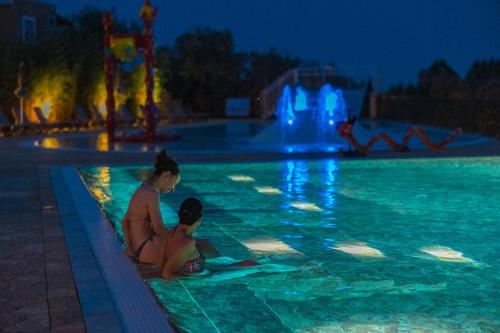 a woman and child sitting in a swimming pool at night at Camping Village Riva Blu in Padenghe sul Garda