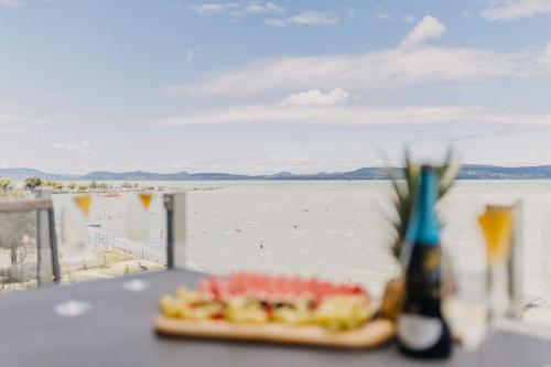 a plate of food on a table with a view of the water at LelleMarine by BLTN Apartmanok Balatonlelle in Balatonlelle