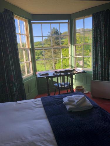 a bedroom with a bed and a table and windows at Bron-Y-Graig in Corwen