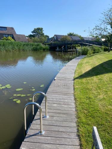 eine hölzerne Promenade neben einem See mit einem Haus in der Unterkunft Wetterwillefriesland in Wommels