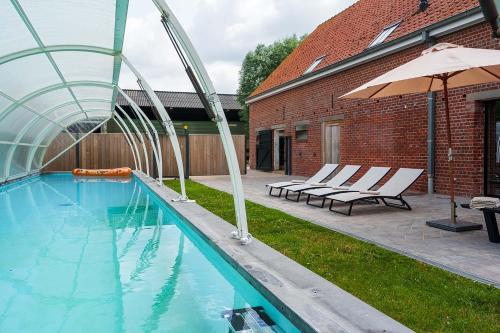 a swimming pool with chairs and an umbrella next to a building at Hulstehof in Zarren