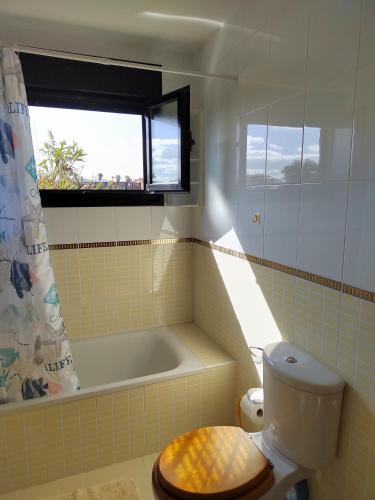 a bathroom with a tub and a toilet and a window at Adam Home Origo Mare in Lajares