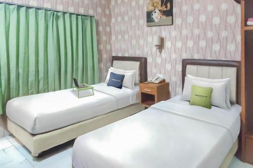 two beds in a hotel room with green curtains at Hotel Syariah Citra Nusantara Balikpapan in Klandasan Kecil