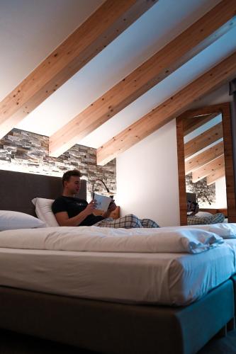 a man sitting on a bed reading a book at Wellness Hotel Lupo Bianco in Canazei