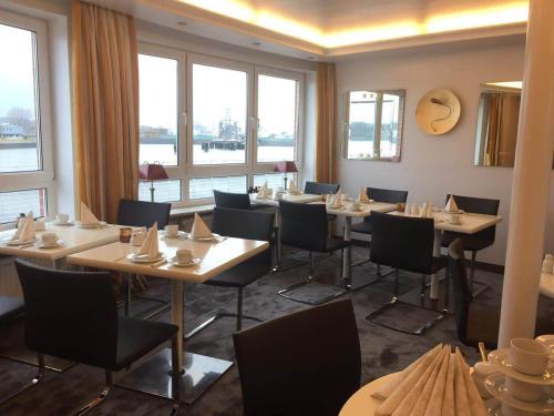 a dining room with tables and chairs and windows at Hotel AM ELBUFER in Hamburg