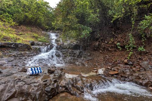 a stream with a water bottle laying on the rocks next to a waterfall at SaffronStays Aranya Vilas & Raanwaara Cottage in Āmbavna