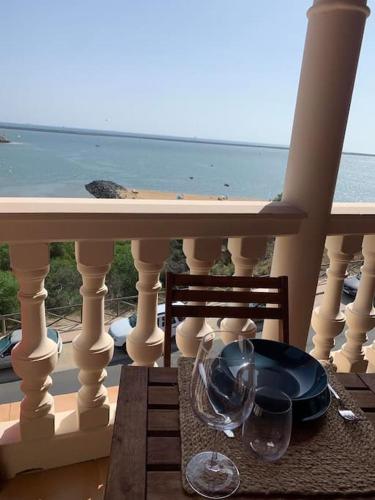 a table with wine glasses on a balcony with the ocean at Hispalis Mazagón Beach 304 in Mazagón