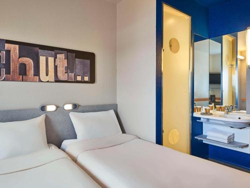 Habitación con 2 camas, lavabo y espejo. en ibis budget Velizy en Vélizy-Villacoublay