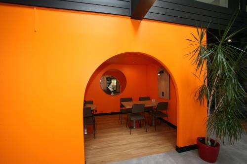 an orange wall with a table and chairs at ibis Saint-Lô in Saint Lo
