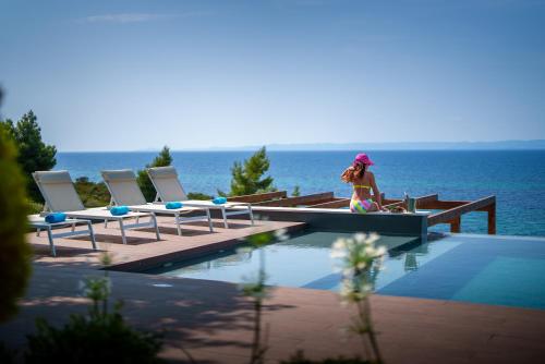 a woman sitting on a bench next to a swimming pool at SEA VIEW Ranch By the Sea in Vatopedi