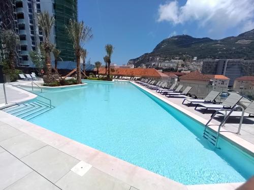 una piscina con sillas y montañas en el fondo en BRAND NEW - Studio Apartments in EuroCity - Large Pool - Rock View - Balcony - Free Parking - Holiday and Short Let Apartments in Gibraltar en Gibraltar