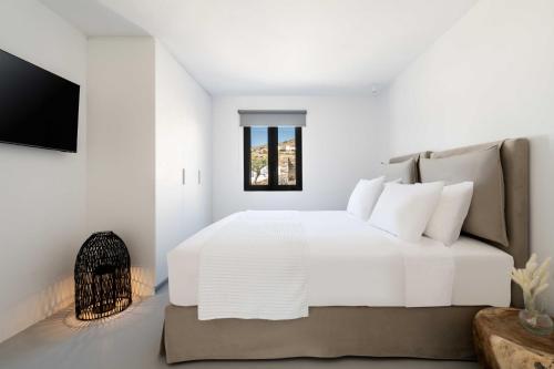a white bedroom with a white bed and a window at Aura Villas Tinos in Agios Romanos