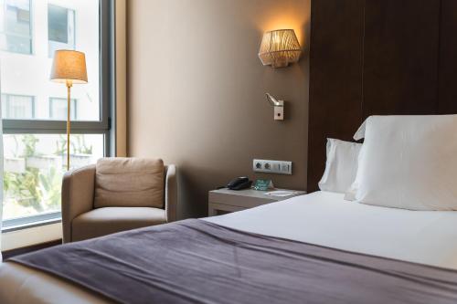 a bedroom with a bed and a chair and a window at La Laguna Gran Hotel in La Laguna