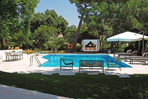 a swimming pool with benches and a table and umbrella at Villa Oasis with Large Pool Athenian Riviera Lagonissi in Lagonissi