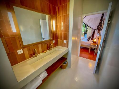 a bathroom with a sink and a mirror and a bed at Maison Ylang Dive Center in Nosy Be