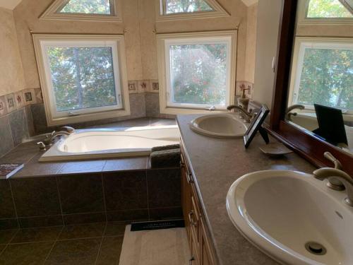 uma casa de banho com 2 lavatórios, uma banheira e 2 janelas em Algonquin Island 'Luxe' Cottage at the edge of the Park em South River