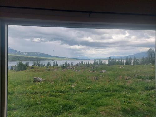 a view from a window of a field with a lake at small camping cabbin with shared bathroom and kitchen near by in Hattfjelldal