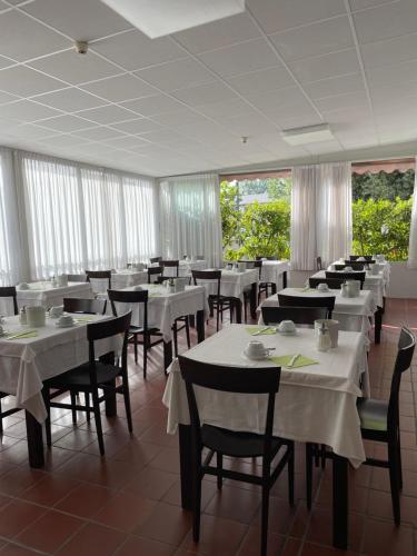 a restaurant with white tables and chairs and windows at Pensione Ornella in Lignano Sabbiadoro