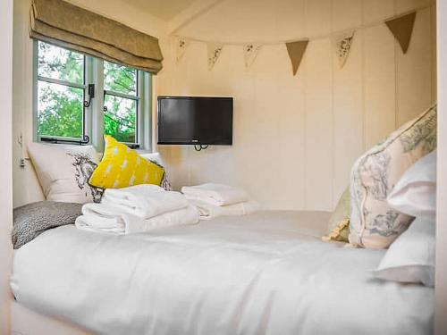 Elle comprend un grand lit blanc avec des oreillers et une télévision murale. dans l'établissement Helens Shepherds Hut, à Enford