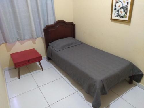 a small bed in a room with a red table at Pousada Dom Aquino in Campo Grande