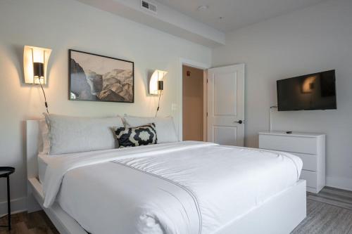 a white bedroom with a large white bed and a flat screen tv at Piedmont Place Suite 304 - near vineyards! in Crozet