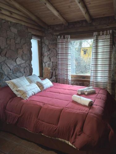 a large red bed in a room with a stone wall at Rincón Alto Cabañas in Nono