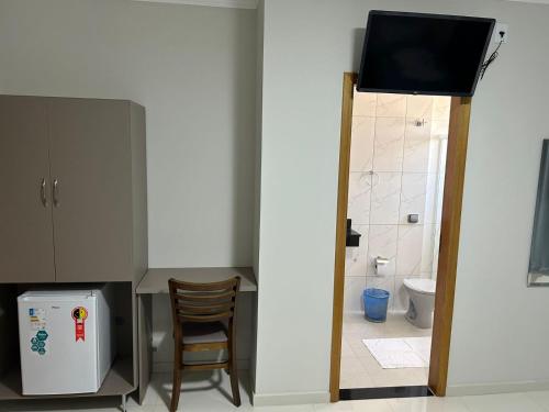 a bathroom with a television and a kitchen with a chair at Hotel Beirut in Aparecida