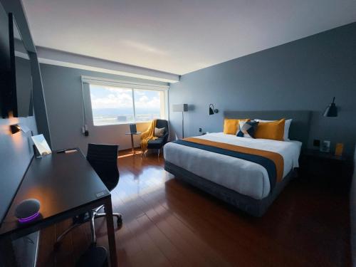 a bedroom with a bed and a desk and a window at Hotel Opus Grand Toluca Aeropuerto in Toluca