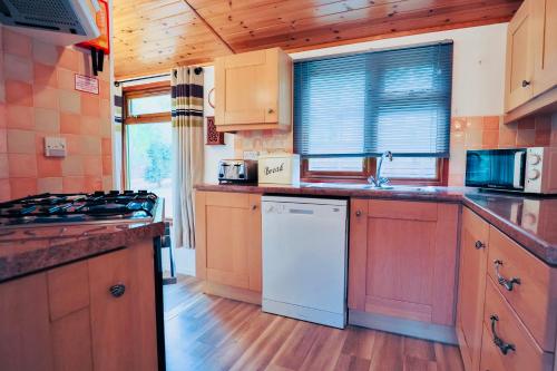 a kitchen with wooden cabinets and a white dishwasher at Rustic Fawn Lodge with Hot Tub for 4 - Resort Spa in Devon in Chudleigh