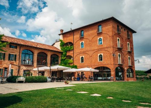 un grande edificio in mattoni con tavoli e ombrelloni di Tenuta Montemagno Relais & Wines a Montemagno