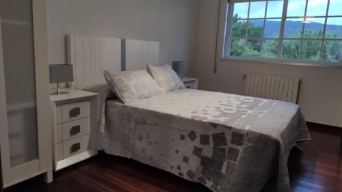 a bedroom with a bed with a night stand and a window at Os piñeiros vacacional in Moaña