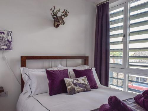 a bedroom with a bed with purple pillows and a window at Bluebell Barn in Grampound