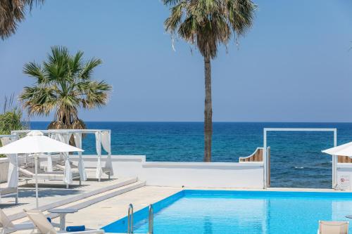 a swimming pool next to the ocean with palm trees at Thalasses in Adelianos Kampos