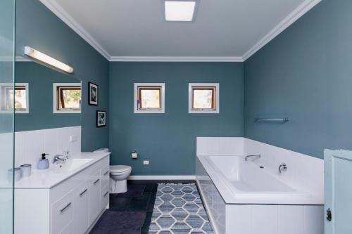 baño azul con bañera, lavabo y aseo en Booroolgunyah Luxury Farm Stay, en Booroolite