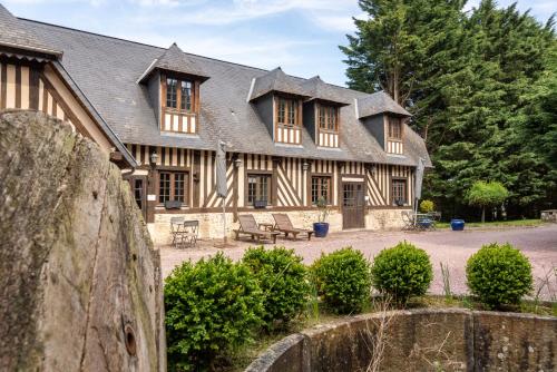 une grande maison en bois avec des bancs devant elle dans l'établissement Gites - Domaine de Geffosse, à Pont-l'Évêque