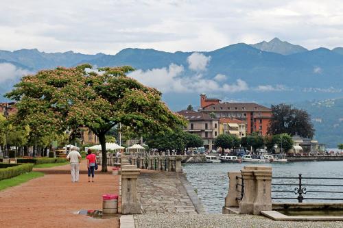a couple of people walking down a sidewalk next to a body of water at MagicView Baveno apartment with garden and lake view in Baveno