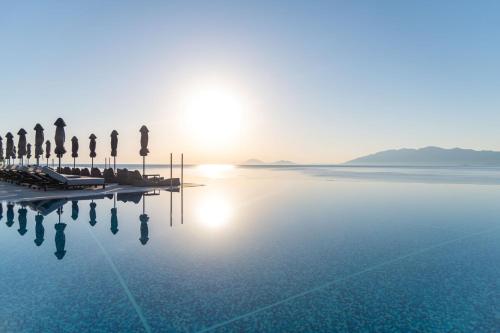 un bassin d'eau avec des palmiers et le soleil dans l'établissement Michelangelo Resort & Spa, à Ágios Fokás