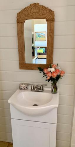a bathroom sink with a mirror and a vase of flowers at North Shore Garden Studio in Haleiwa