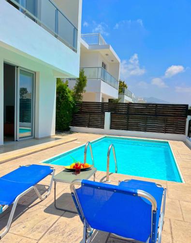 a swimming pool with two chairs and a table next to a house at 3 Bedroom Coral Bay Beach Seaview Villa I Private Pool in Peyia