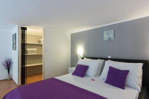a bedroom with a large bed with purple and white pillows at Apartments Storia in Trogir
