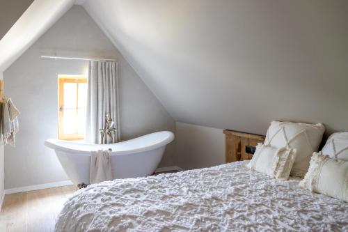 a white bedroom with a bed and a bath tub at 't Hooiland in Lo-Reninge