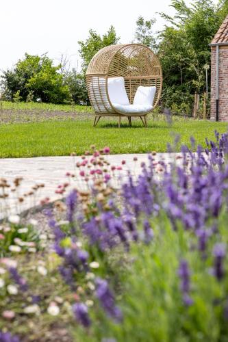 a wicker chair sitting in a garden with flowers at 't Hooiland in Lo-Reninge
