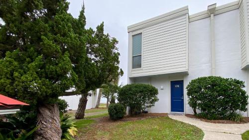 una casa blanca con una puerta azul y árboles en VILLA 176 - Villa Delmar condo en Jekyll Island